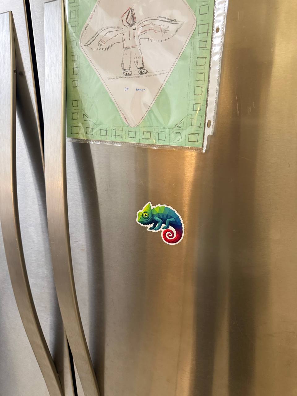 Chameleon magnet on a fridge next to kid art