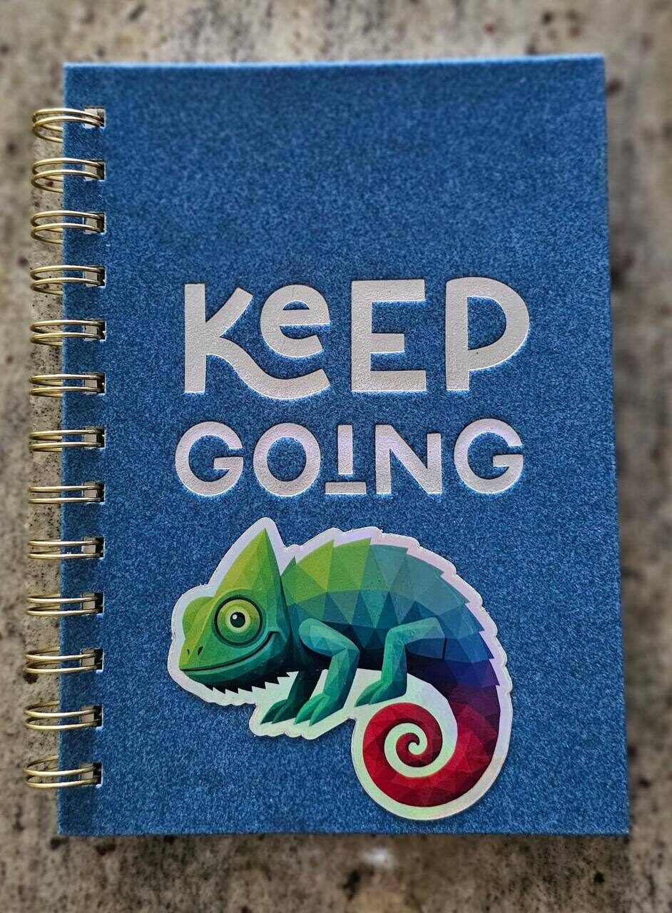 Chameleon sticker on a blue Keep Going spiral notebook